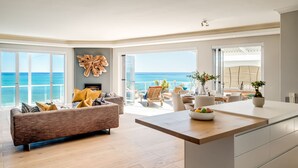 Un ampio soggiorno con una grande finestra vista oceano, una cucina moderna con isola in legno e un balcone con posti a sedere all'aperto.