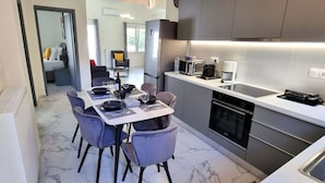 Une cuisine moderne avec un coin repas, dotée d’un sol en marbre, de chaises grises et d’appareils électroménagers contemporains.