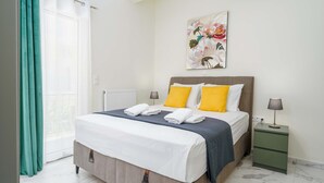 Un lit bien fait, avec des oreillers blancs et jaunes, une tête de lit grise et une table de chevet verte sur laquelle se trouve une lampe.
