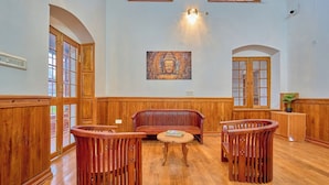 Una habitación con suelo de madera, un sofá rojo, dos sillas de madera, una pequeña mesa redonda y un cuadro de Buda en la pared.