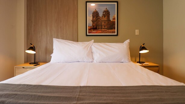 A neatly made bed with white linens, two bedside lamps, and a framed picture of a building on the wall. - w Magnificent 3BR in the Heart of Barranco (Lima)