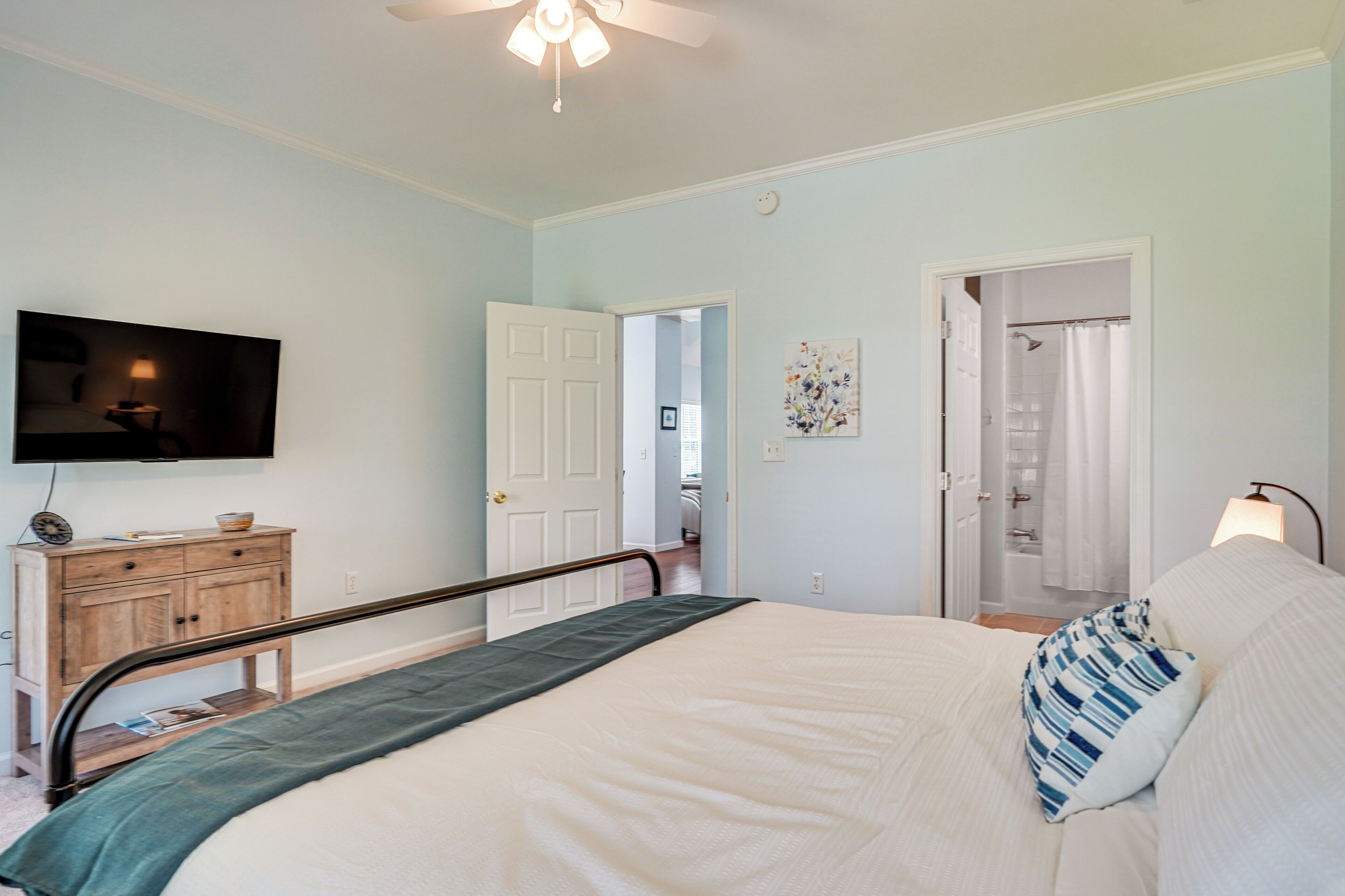 A bedroom with a bed, a wooden nightstand, a television, and a door leading to another room.