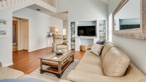 A spacious living room with a high ceiling, a comfortable beige sofa, a wooden coffee table, and a television mounted on the wall. - Walk to Bay & Dtwn: Port St Joe Paradise w/ Grill! (Port St. Joe)