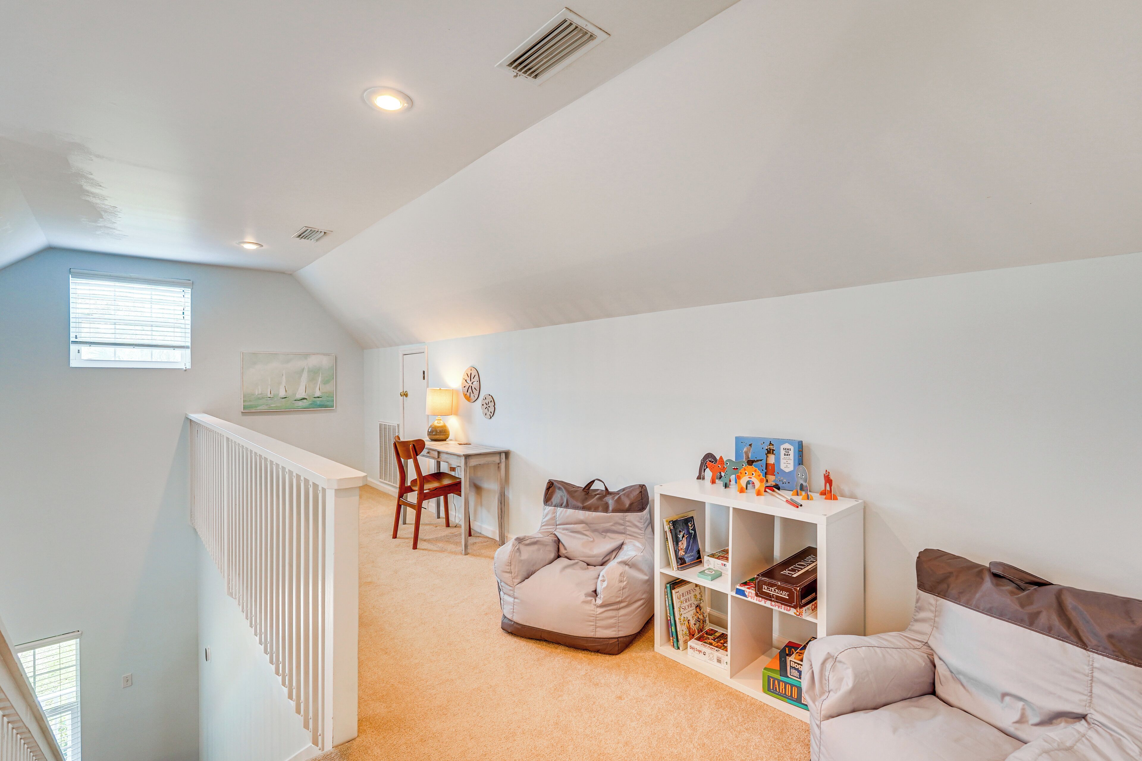 A spacious room with a high ceiling, a white staircase, a desk with a chair, a bean bag chair, and a bookshelf.