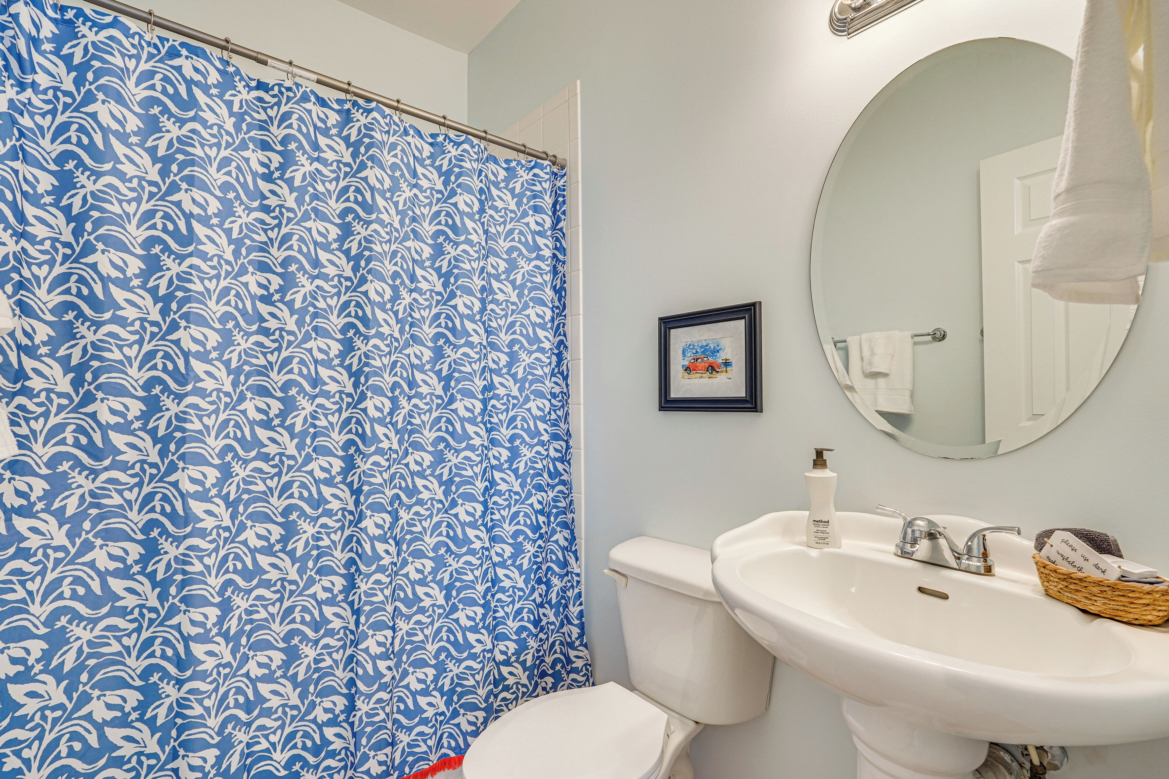 A bathroom with a white toilet, a sink with a bottle of soap, and a framed picture on the wall.