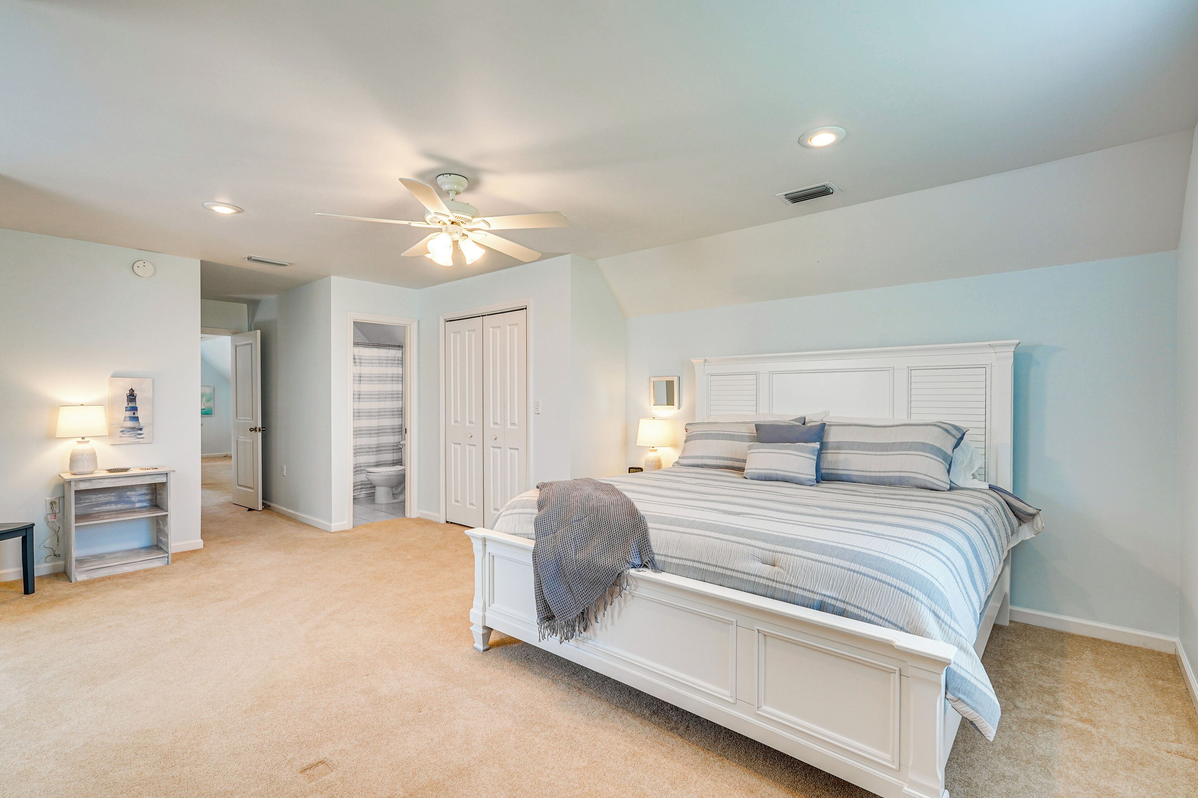 A bedroom with a large bed, a ceiling fan, and a light fixture.