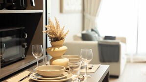 A dining area with a table set for four, including bowls, plates, glasses, and cutlery. A microwave and oven are visible in the background. - WelHome - LOCI Residences (Dubai)