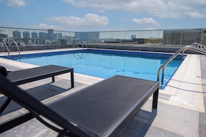 A rooftop pool with clear blue water, metal railings, and a city skyline view in the background. - WelHome - LOCI Residences (Dubai)