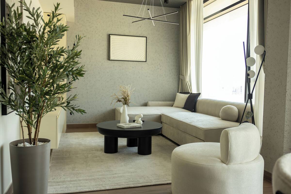 A modern living room with a large potted plant, a round coffee table, a sofa, and a minimalist wall art piece.