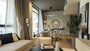 A modern living room with a sofa, coffee table, and decorative items. There is a dining area with a table and chairs in the background. - WelHome - LOCI Residences (Dubai)