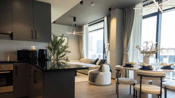 A modern kitchen with a central island, a dining area with a round table and chairs, and a seating area with a sofa and a coffee table. - WelHome - LOCI Residences (Dubai)