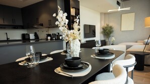 A modern dining area with a dark wooden table set for two, featuring black bowls, white napkins, and clear wine glasses. - WelHome - LOCI Residences (Dubai)