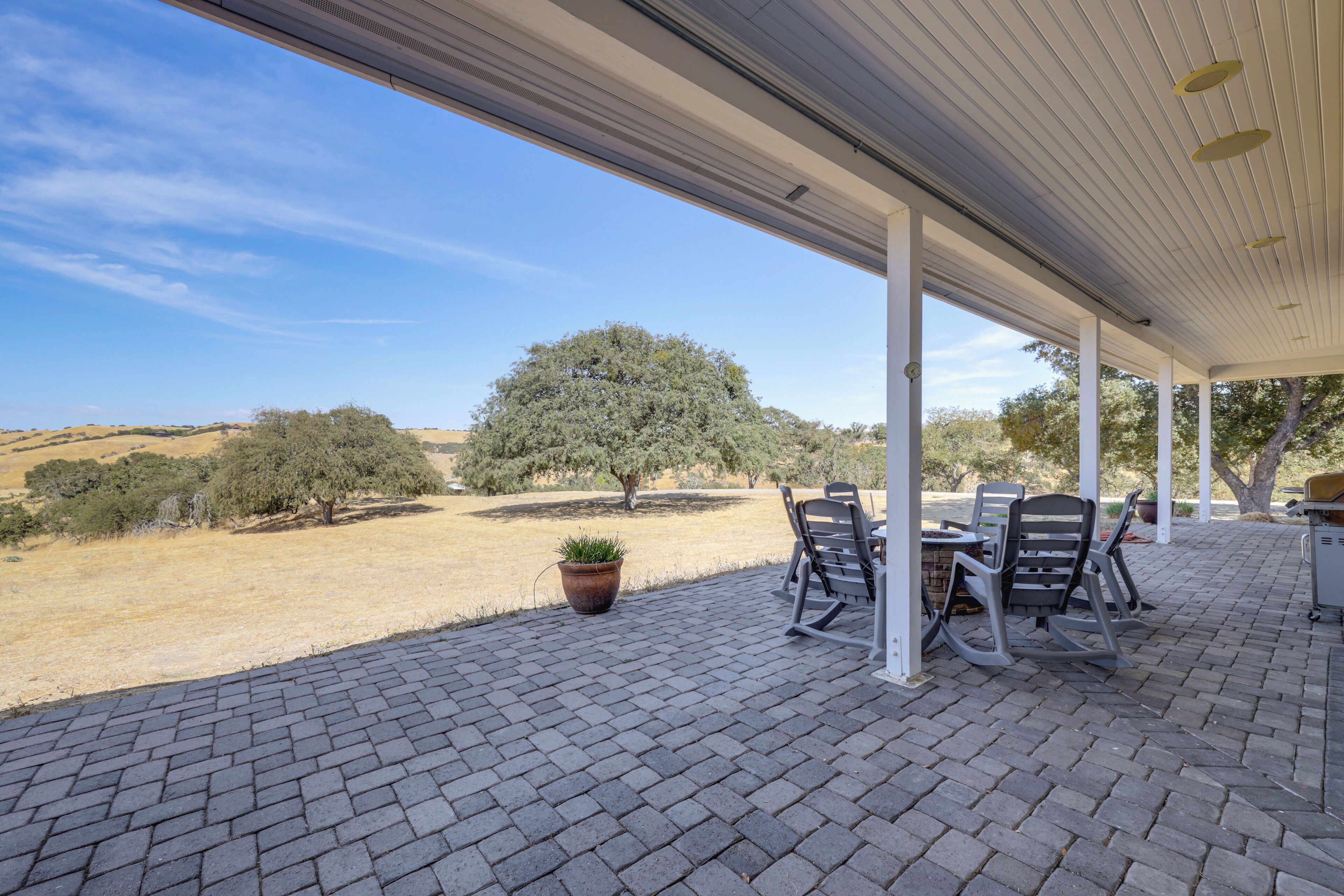 An outdoor patio with a brick floor, white columns, and a table with chairs.