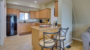 A kitchen with wooden cabinets, a stainless steel refrigerator, and a granite countertop. There are two bar stools and a coffee maker on the counter. - A-frame w/ Patio & Mtn Views: Arizona Retreat (Apache Junction)