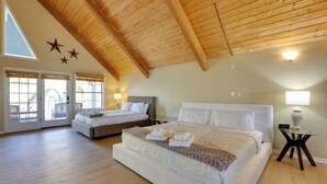 Ein geräumiges Schlafzimmer mit zwei Betten, Holzbalkendecke und einem großen Fenster mit Jalousien.