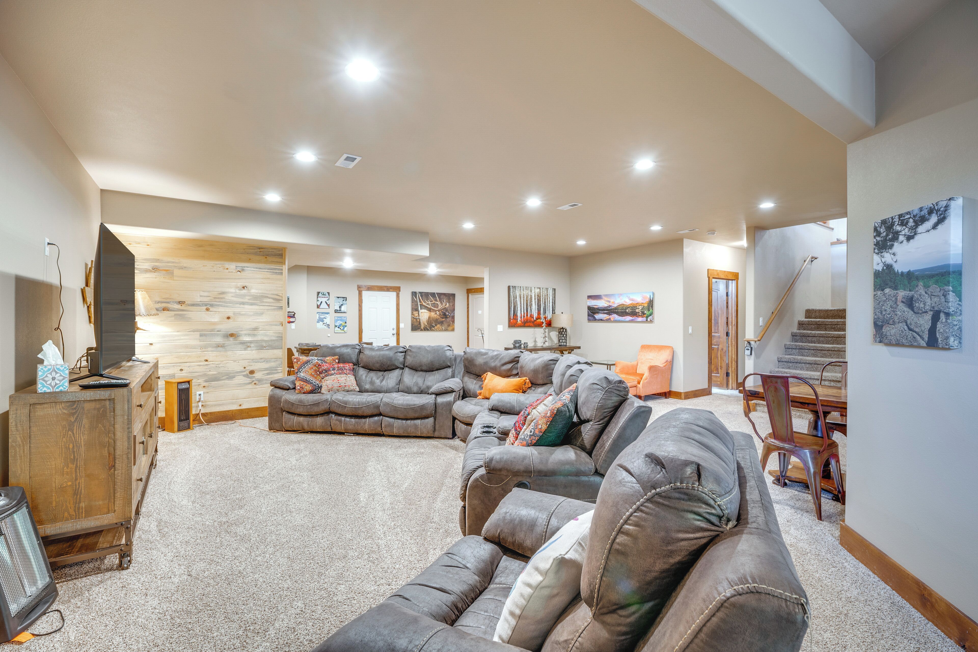 A spacious living room with a large sectional sofa, a wooden accent wall, and a staircase leading to an upper level.