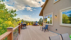 Eine Holzterrasse mit Sitzgelegenheiten und großen Fenstern mit Blick auf ein bewaldetes Gebiet.