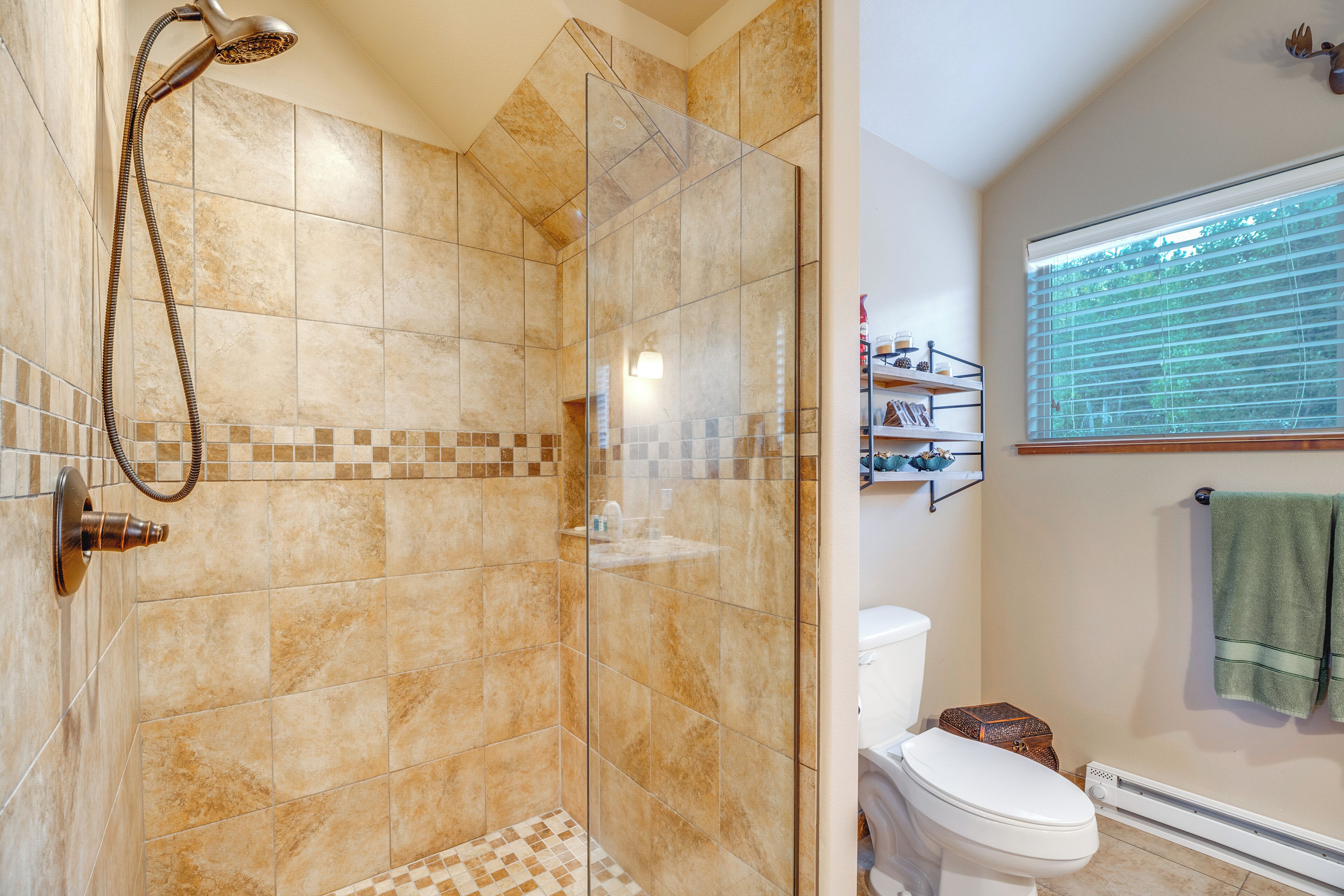 A bathroom with a glass-enclosed shower, a toilet, and a window with blinds.
