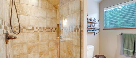 A bathroom with a glass-enclosed shower, a toilet, and a window with blinds.