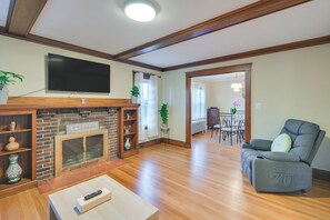 A living room with a fireplace, a television mounted on the wall, a sofa, and a dining area in the background. - Belmont Home < 3 Mi to Harvard Square! (Belmont)