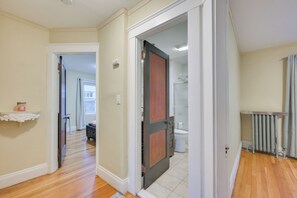 A hallway with wooden flooring, a door leading to a bathroom, and a radiator on the right. - Belmont Home < 3 Mi to Harvard Square! (Belmont)