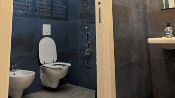 Ein Badezimmer mit Steinwand, Toilette, Bidet und Waschbecken mit Spiegel.
