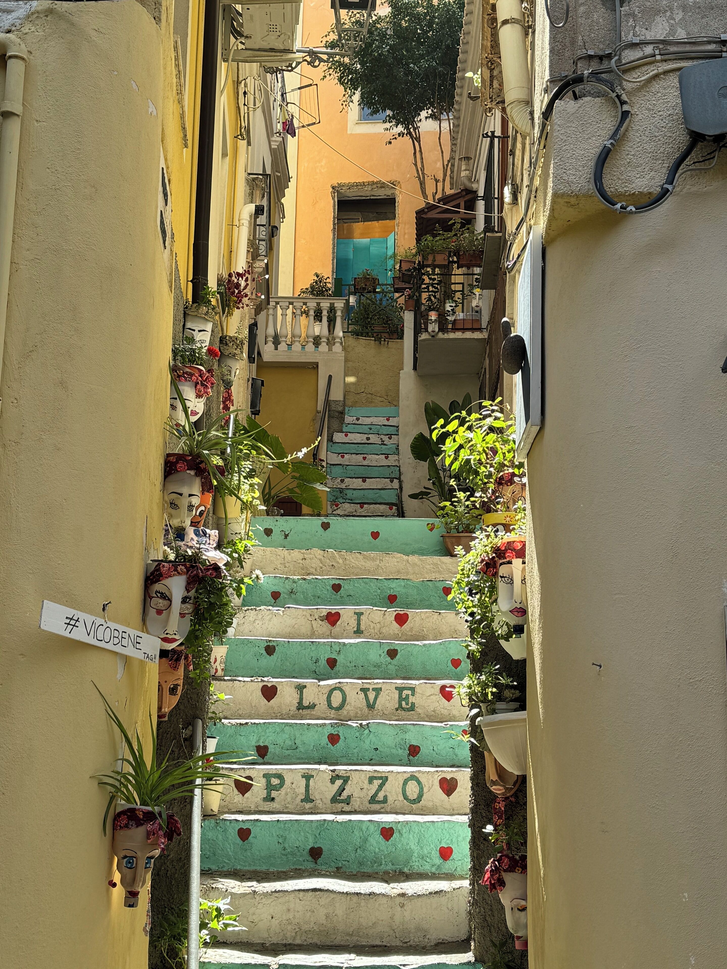 Un vicolo stretto con una scala decorata da piastrelle a forma di cuore che compongono la scritta 'I LOVE PIZZA'.