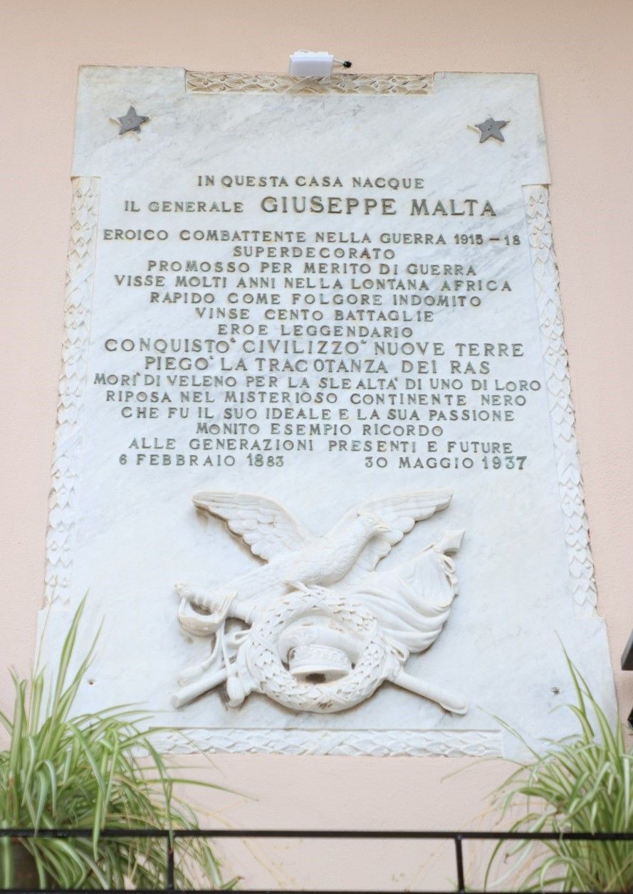 A marble plaque with text commemorating General Giuseppe Malta, highlighting his military achievements and contributions.