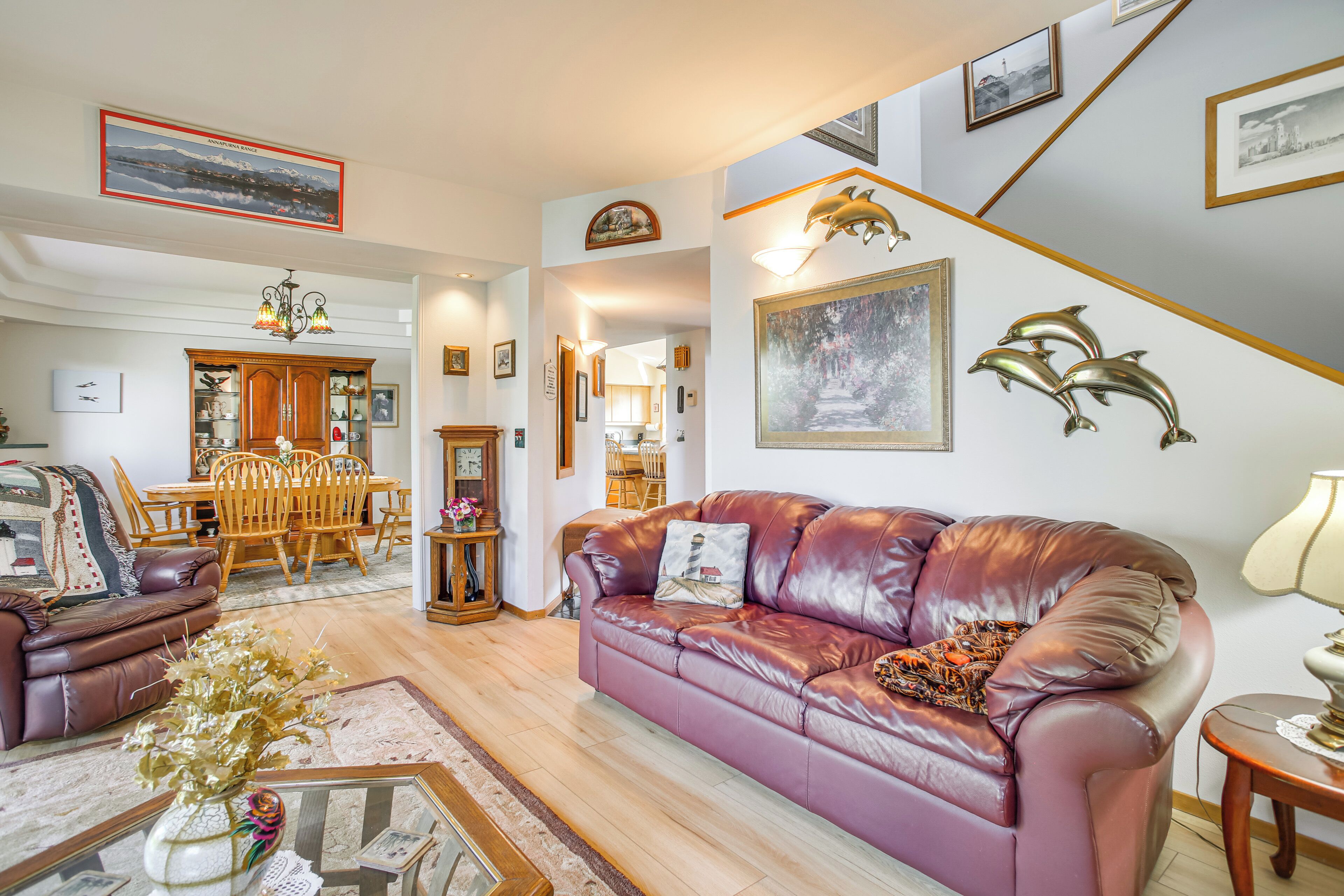 A living room with a leather sofa, a dining area with a wooden table and chairs, and a hallway with framed pictures and a chandelier.