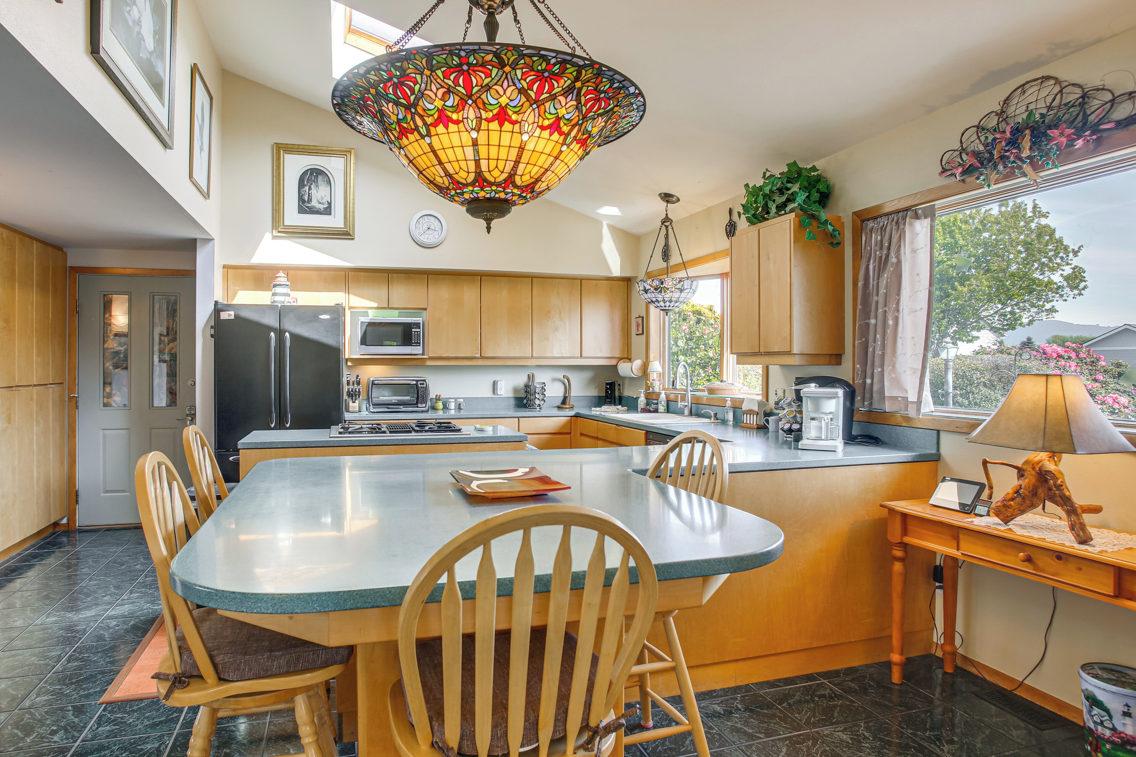 A modern kitchen with a central island, wooden cabinets, a refrigerator, microwave, and a dining area with chairs and a table.