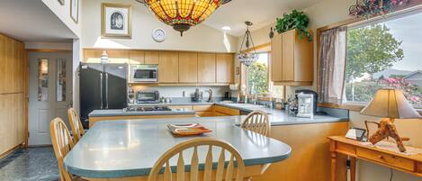 A modern kitchen with a central island, wooden cabinets, a refrigerator, microwave, and a dining area with chairs and a table.