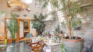 A room with a large potted plant, a wicker basket, a wooden rocking chair, and a stone wall with a built-in fireplace. - Unique Home w/ Beautiful Mtn Views! (Sequim)