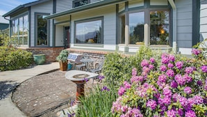 A house with large windows, a patio with outdoor furniture, and a garden with flowers. - Unique Home w/ Beautiful Mtn Views! (Sequim)