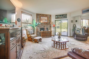 A living room with a fireplace, a television, and a leather sofa. - Unique Home w/ Beautiful Mtn Views! (Sequim)