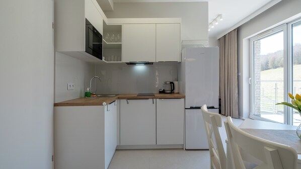 Una cocina moderna con armarios blancos, un refrigerador de acero inoxidable, una cafetera y una ventana con vista a un paisaje verde.