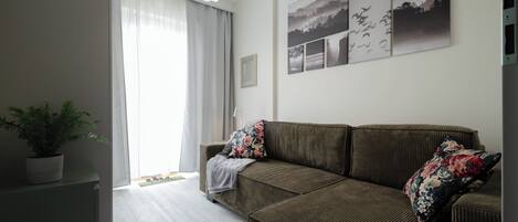 A living room with a sofa, a potted plant, and a wall with framed pictures.