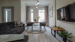 Una sala de estar moderna con un sofá, una mesa de comedor con sillas, un televisor montado en la pared y una planta en maceta.