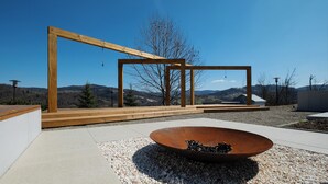 Un espacio exterior moderno con una pérgola de madera, un cuenco metálico grande y vistas a colinas distantes.