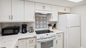 A compact kitchen with white cabinets, a microwave, a coffee maker, a toaster, a stove, and a refrigerator. - B-116 - Resort Views and Close to the Lobby (Naples)