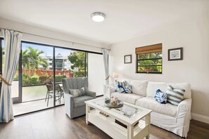 Een woonkamer met een glazen schuifdeur die leidt naar een balkon, een witte bank, een grijze fauteuil en een salontafel.