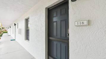 A building exterior with a dark door, a number plaque '116', and a covered walkway.