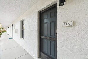 L’extérieur d’un immeuble avec une porte sombre, une plaque portant le numéro « 116 », et une allée couverte.