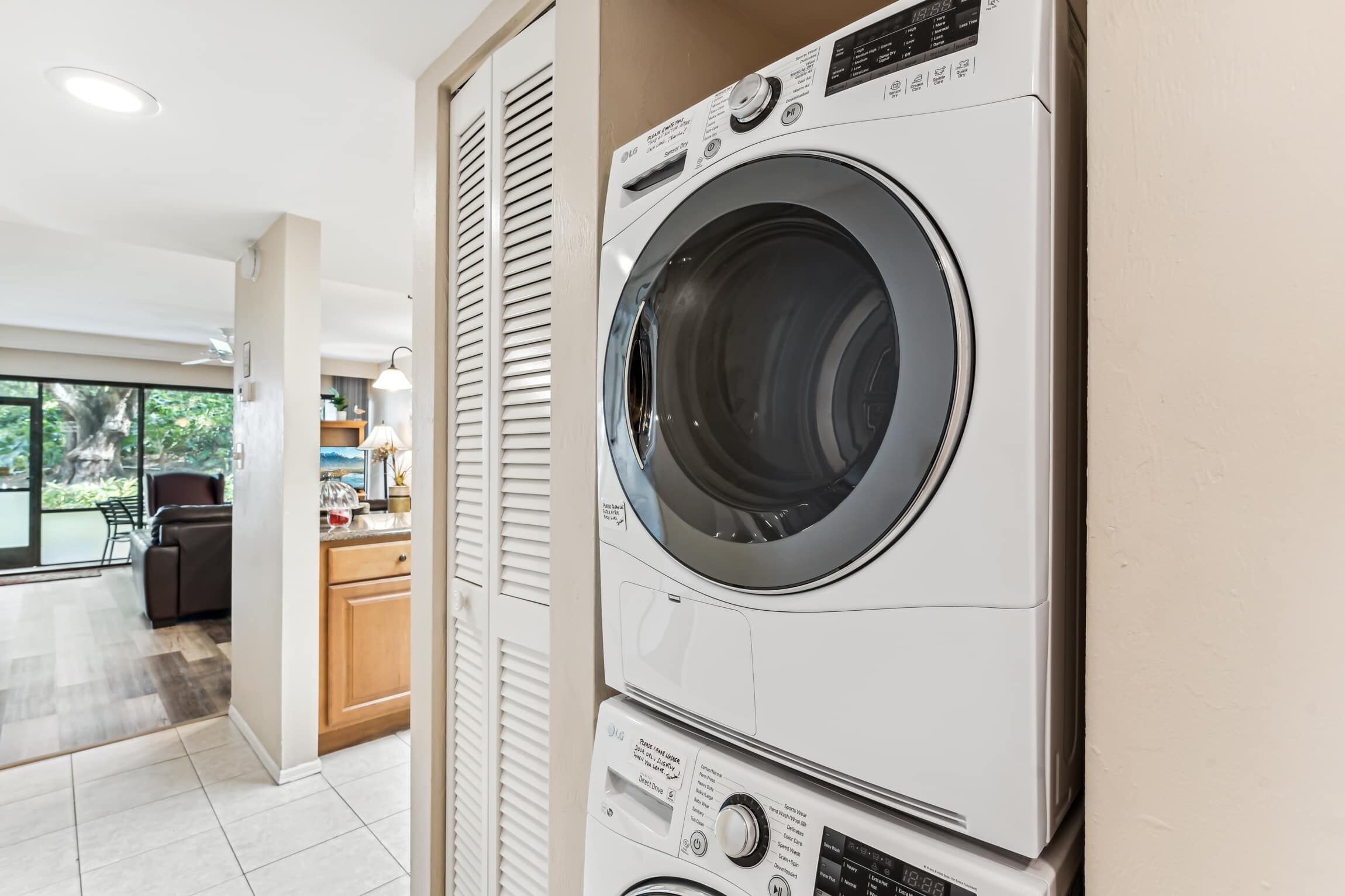 A modern laundry room with a front-loading washer and dryer, a kitchen area, and a view of the outdoors.