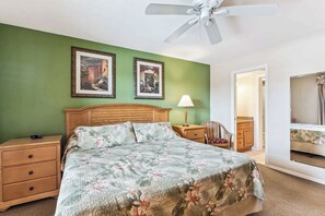 A bedroom with a wooden bed, green walls, two framed pictures, a nightstand, a lamp, a chair, and a ceiling fan. - D-126 Resort Views, Quiet Back End of Resort (Naples)