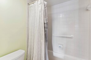 A bathroom with a toilet, a shower with a white tiled wall, and a white shower curtain.