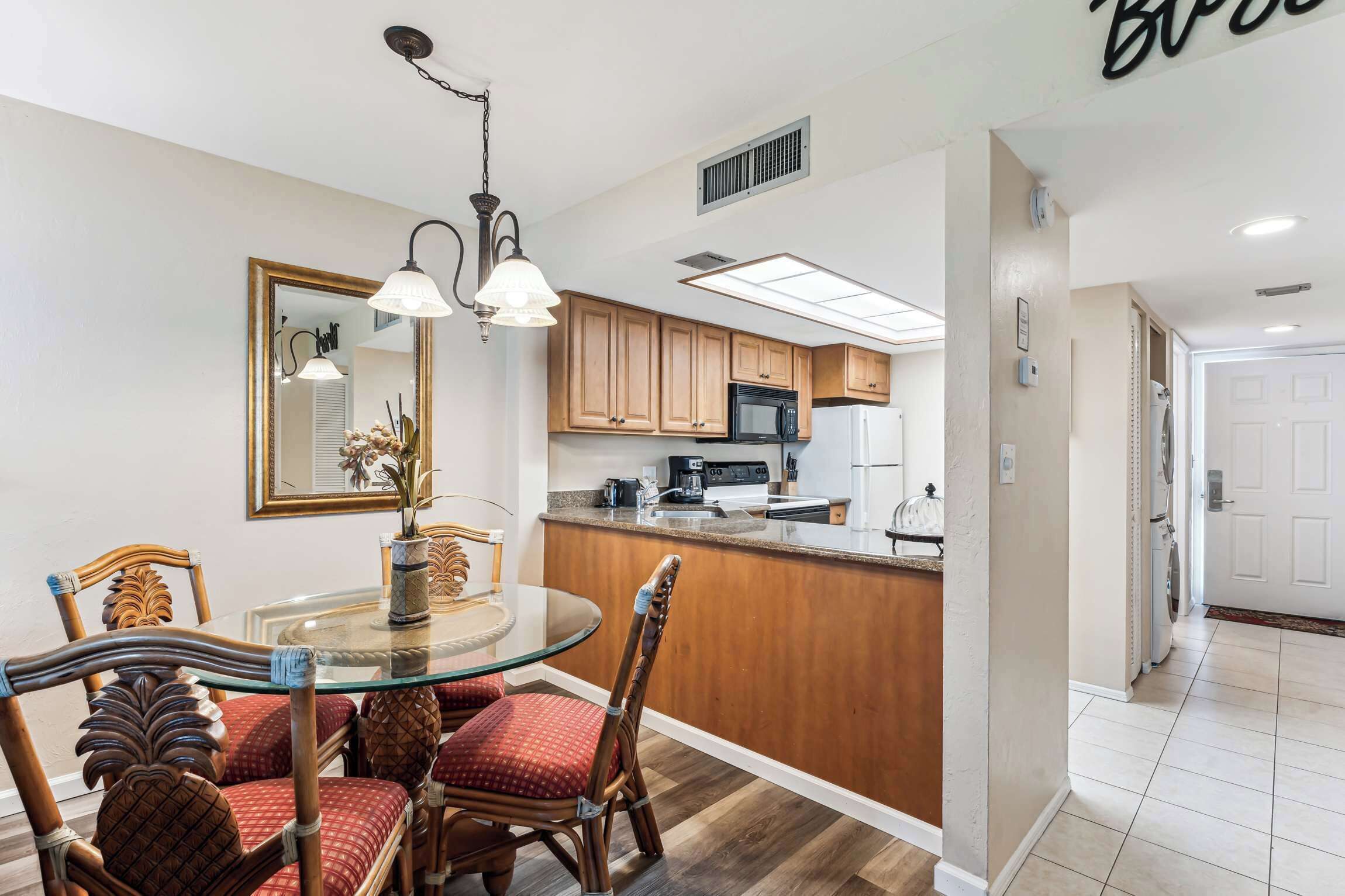 A modern kitchen with wooden cabinets, a central island, and a dining area with a glass table and wicker chairs.