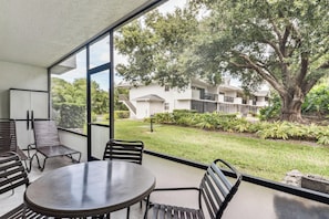A balcony with a table and chairs, overlooking a well-maintained garden and a building with multiple balconies. - D-126 Resort Views, Quiet Back End of Resort (Naples)