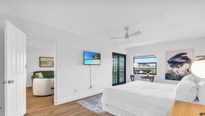 Een moderne slaapkamer met een groot bed, een televisie, een plafondventilator en uitzicht op het omliggende landschap door een raam.
