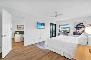 A modern bedroom with a large bed, a TV, a ceiling fan, and a view of the outdoors through a window. - F-335 - Modern Interior, 3rd Floor, Privacy (Naples)