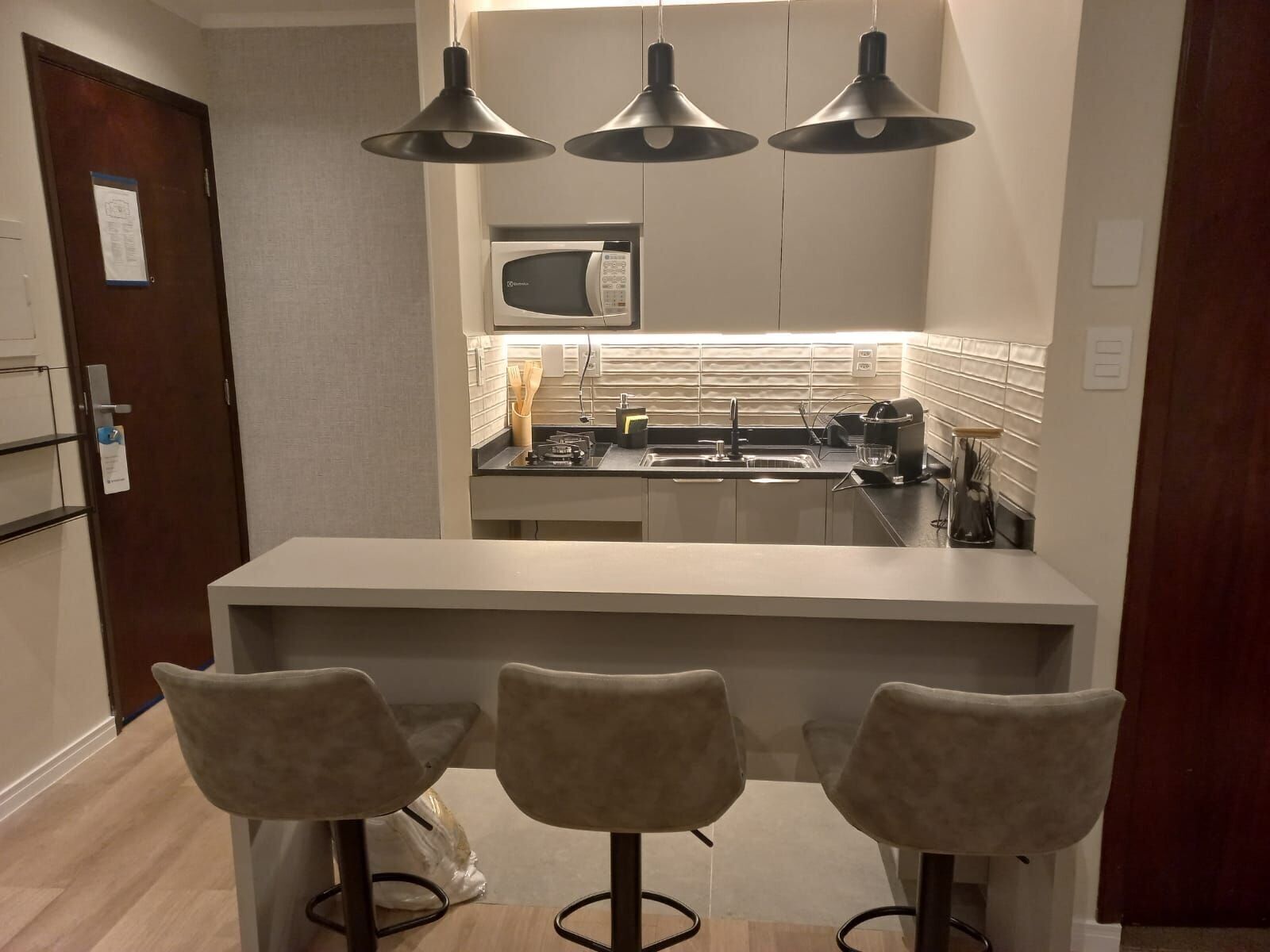 A compact kitchen with a microwave, stove, and modern pendant lights. There are three bar stools and a small island.